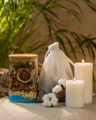 A table displays a jar of herbs salts and dried fruits, a candle, and cotton bag full of herbal infusion, creating a tranquil setting ideal for relaxation and self-care rituals.