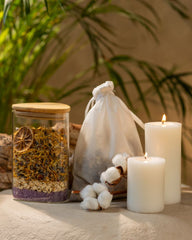 On a table, a jar of herbs, a candle, and cotton bag full of berbs are presented, symbolizing a peaceful environment for rejuvenating bath experiences.